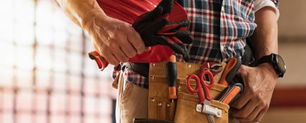 Closeup of bricklayer hands holding hardhat and construction equipment. Detail of mason man hands holding work gloves and wearing tool kit on waist. Handyman with tools belt and artisan equipment.