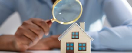 Businesswoman Holding Magnifying Glass Over House Model