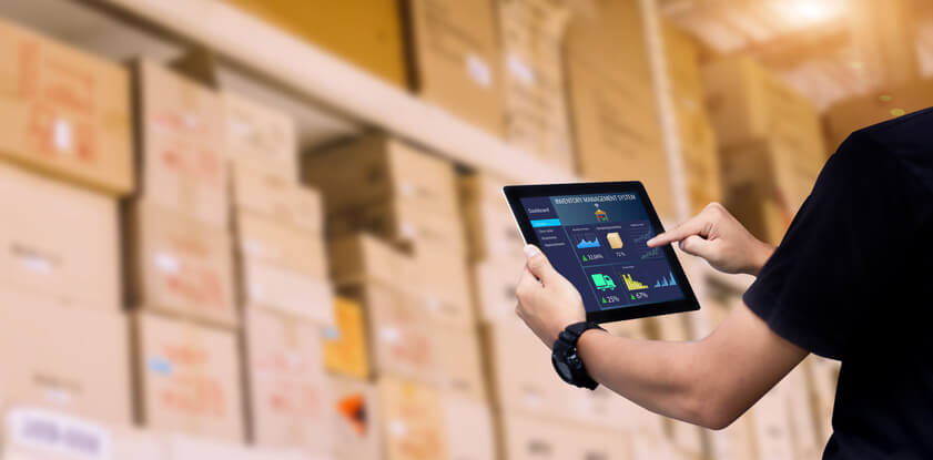 After Logistics Management Training, a logistics manager stands in a warehouse using software on a tablet for an inventory stocktake
