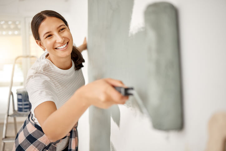Young woman painting a wall at home after Home Renovation Technician Training.