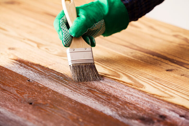 Professional home renovation technician applying paint to a wooden floor surface after home renovation training