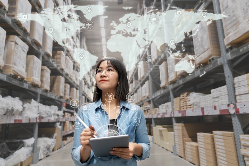 Portrait of a young Asian supply chain management woman looking at inventory in a warehouse using a smart tablet.