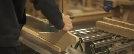 A close-up of a person's hands using a jointer to smooth a piece of wood, which is part of the practical skills acquired during cabinetmaking training