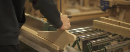 A close-up of a person's hands using a jointer to smooth a piece of wood, which is part of the practical skills acquired during cabinetmaking training