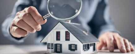 A man holding a magnifying glass over a house model in home inspection training