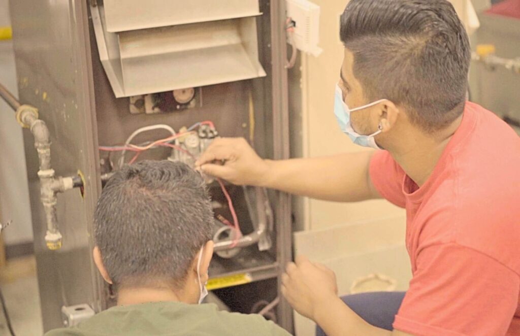 A pair of male HVAC technicians working on a residential HVAC system after completing HVAC technician training