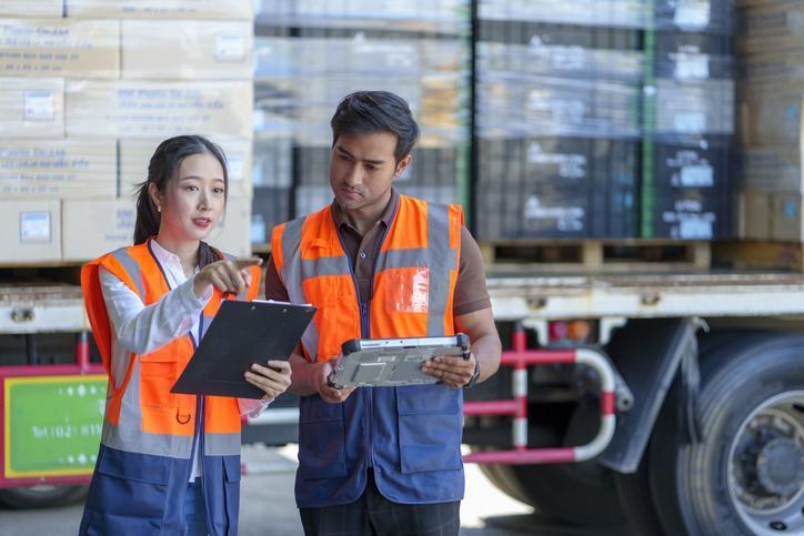 Two logistics managers at a warehouse using a clipboard after logistics management training