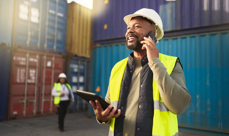 A smiling male logistics professional communicating with a customer over the phone after completing his logistics training