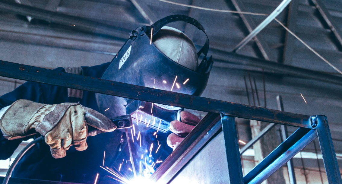 Welder in a protective helmet and gloves welding a metal frame, with sparks flying
