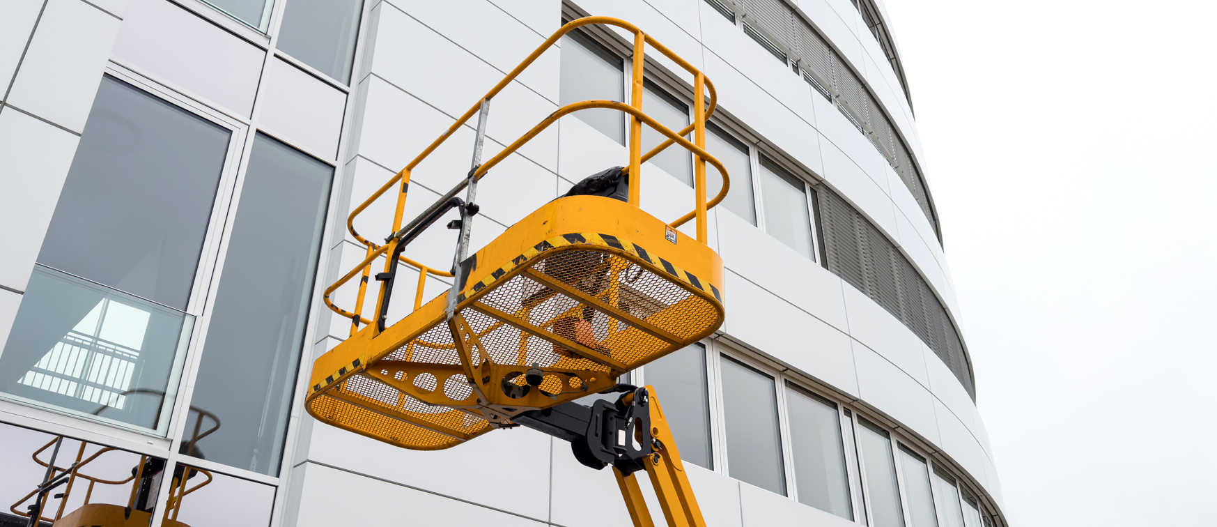 Worker in a yellow aerial lift platform basket raised alongside an office building