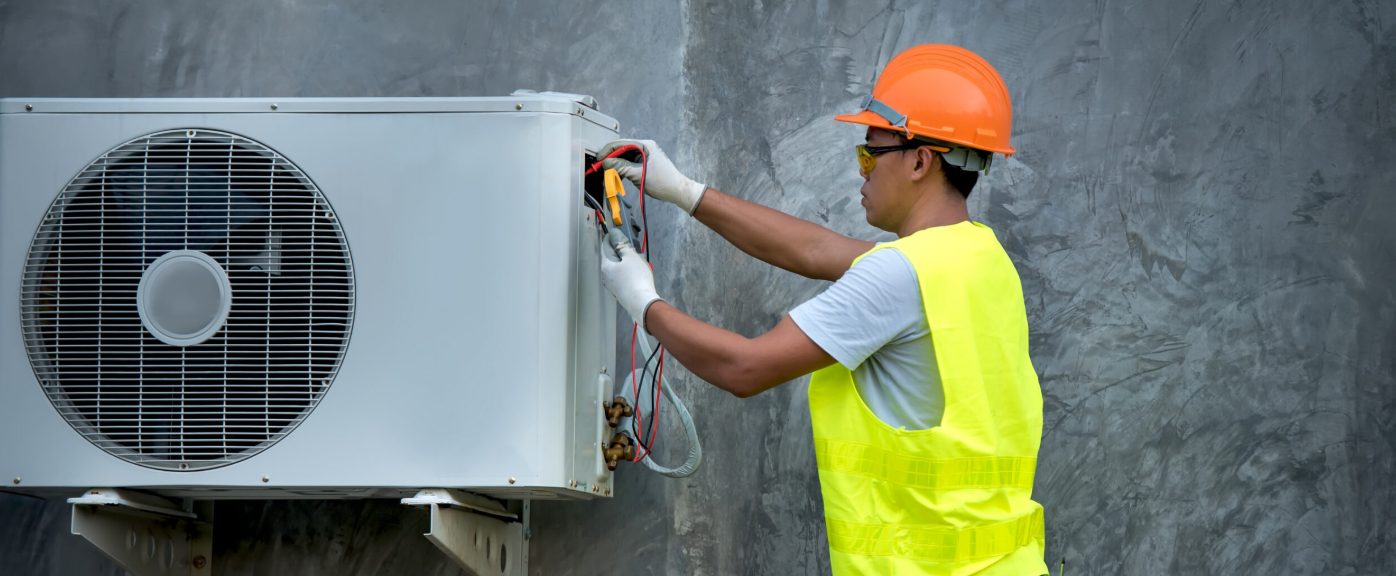 HVAC technician in safety gear testing an outdoor air conditioning unit with a meter